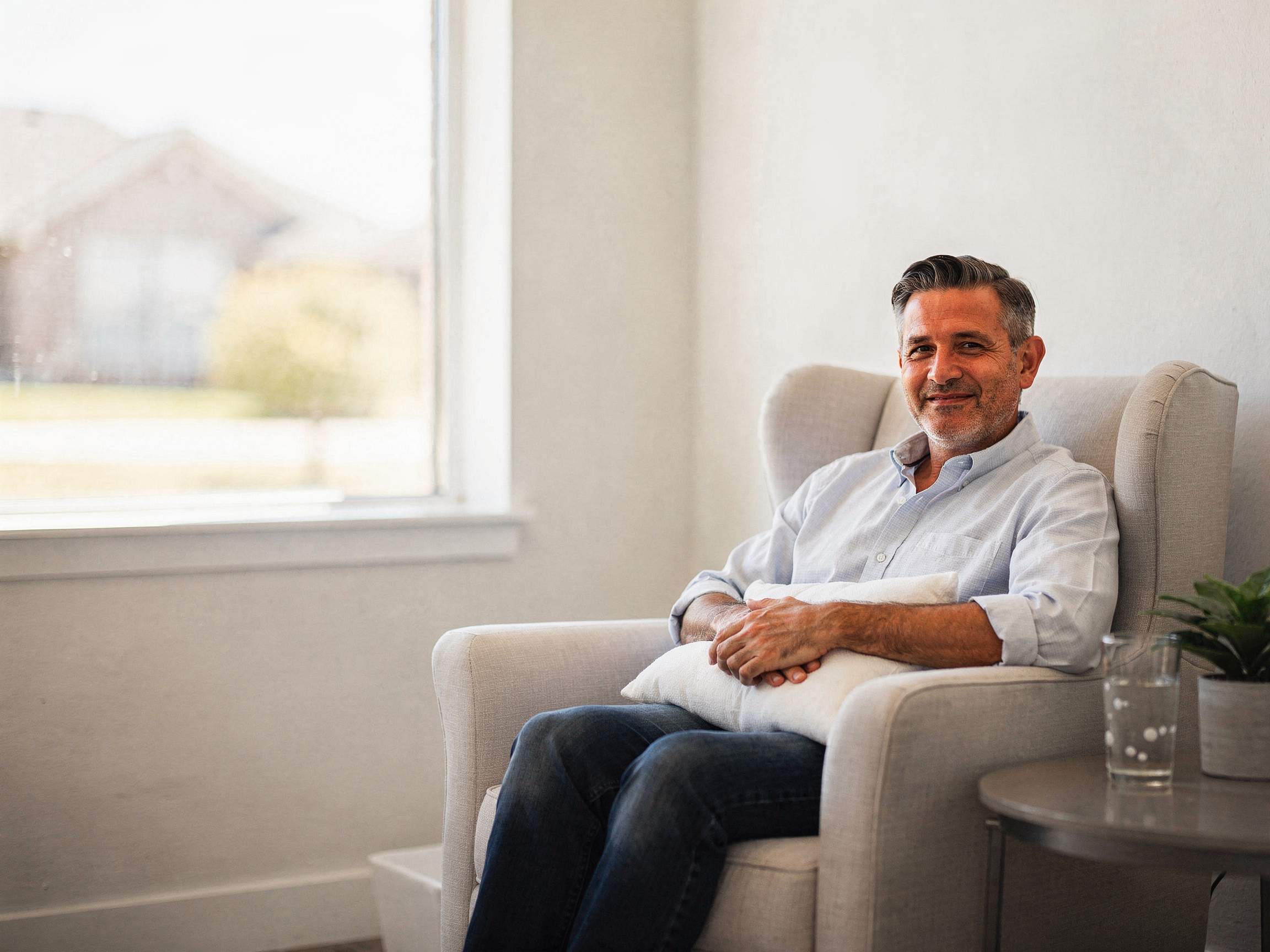 Man sitting in a cream armchair in a bright clinical consultation room, smiling at camera